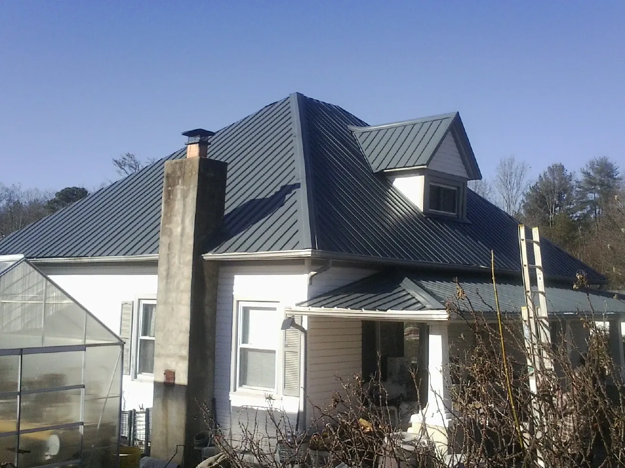 Dark blue standing seam metal roof on a white farmhouse with dormer — Slate & Tile Roof Repair by Roofing Brothers in Cecilia