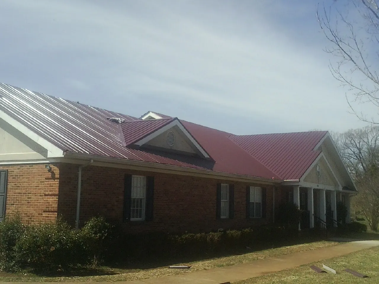 Red metal roof with gabled entries on a long brick building, from a Hail Damage Roof Repair job in Cecilia