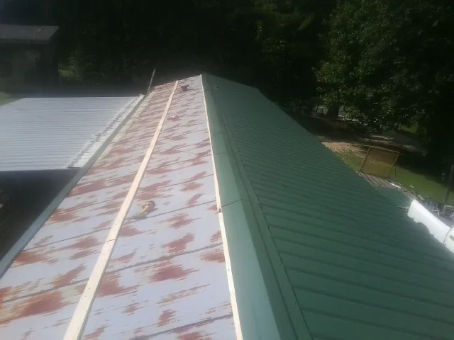 Old rusted panels beside newly installed green metal roofing — Wind Damage Roof Repair by Roofing Brothers in Cecilia