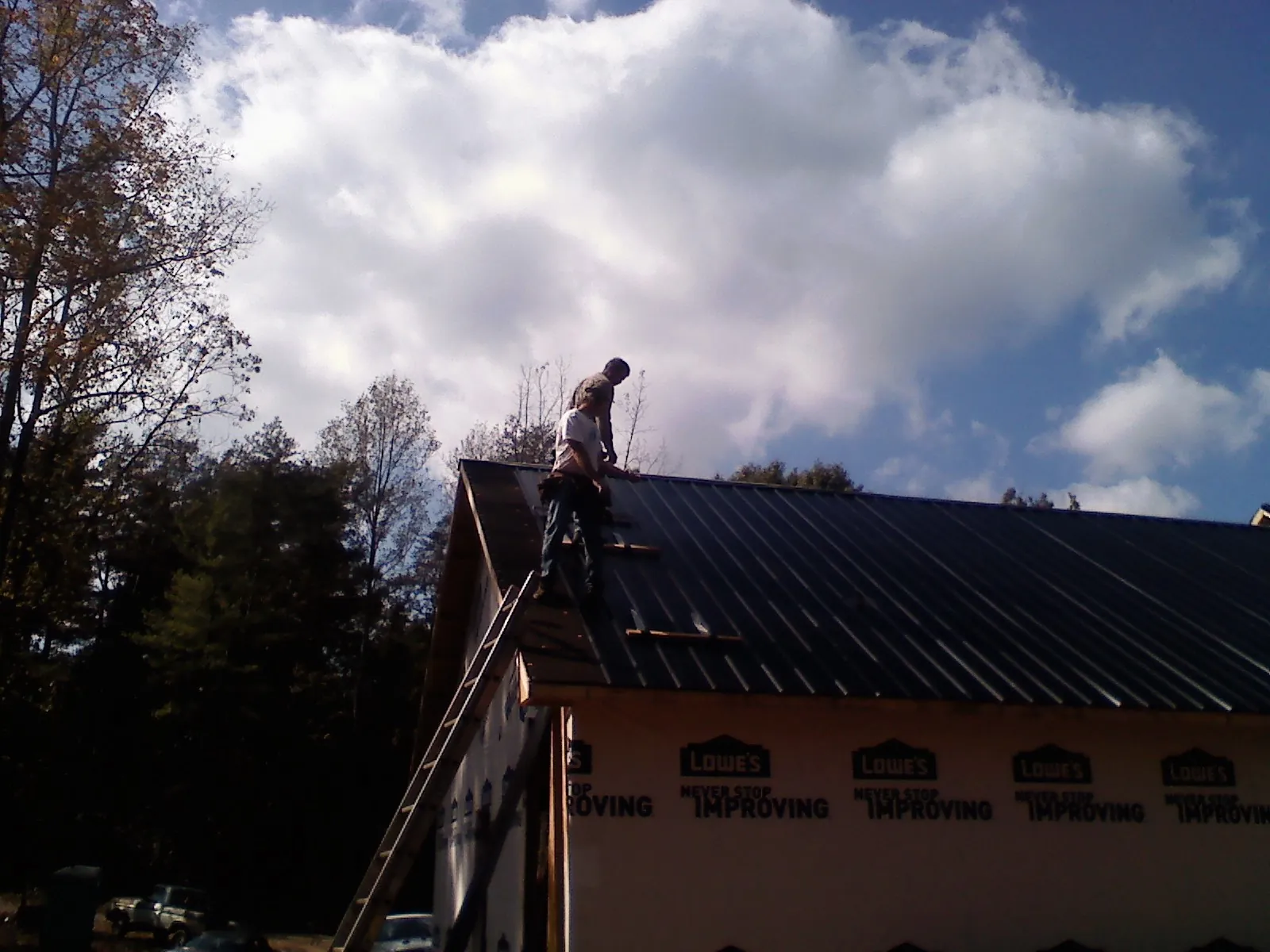 Roofer fastening dark metal panels high against a cloudy sky, from a Roof Inspection job in Cecilia
