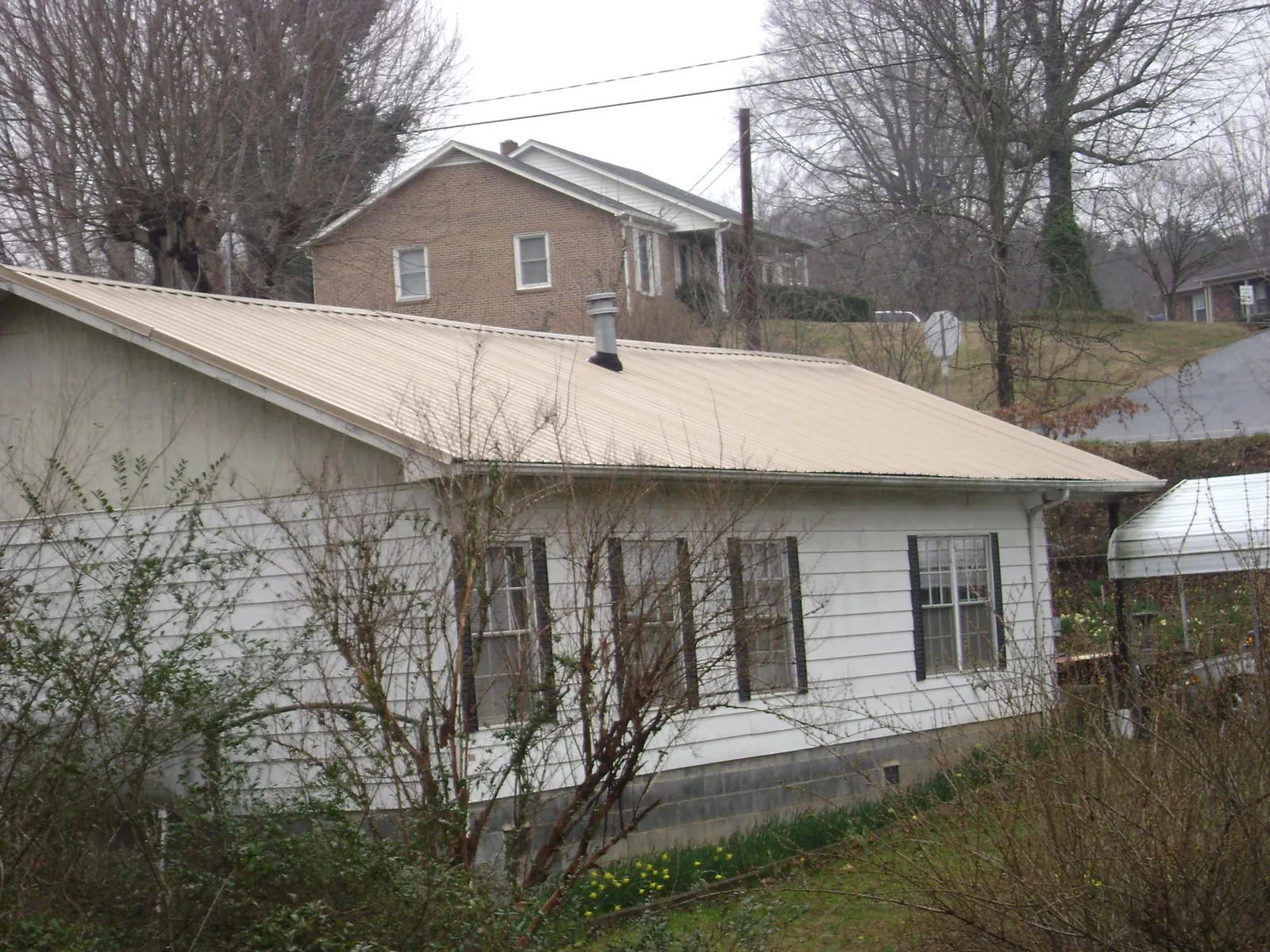 Tan metal roof on a white sided house set into a hillside — Commercial Roofing by Roofing Brothers in Cecilia
